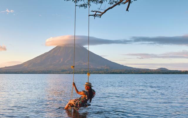 Woman on a swing with Ometepe Volcano on the background